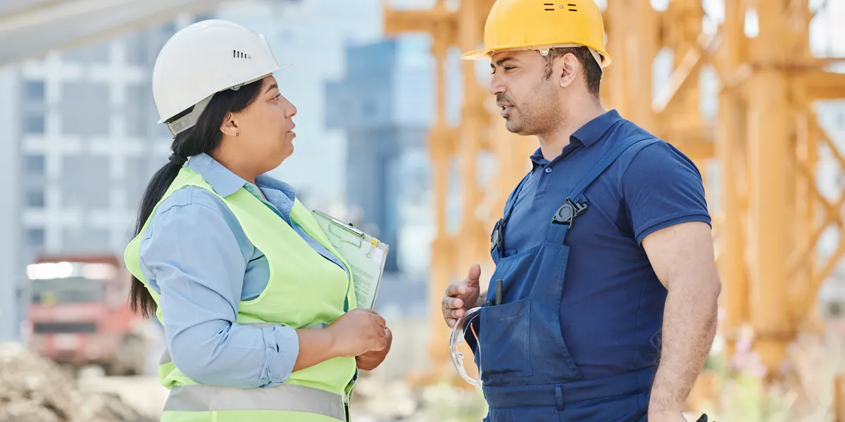 Site workers in hi-vis and hard hats talking in front of a tower crane on an open construction site